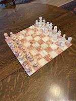 Top view of full chessboard with all pieces arranged for play, showing pink and white onyx squares and pieces.