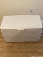 Closed white Coleman cooler showing exterior shape and wooden handles.