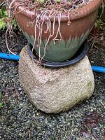 Smaller solid decorative stone with a ceramic pot on top, placed outdoors on gravel.