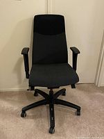 Front view of black and dark grey Donati office desk chair with armrests and five-prong caster base on carpeted floor.