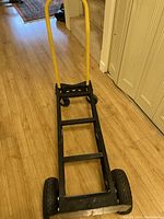 Full view of hand truck mode with yellow handle and black frame on wooden floor