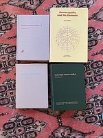 Four homeopathy books placed on a patterned rug surface, showing front covers and titles.