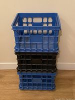 Three stacked plastic file crates, two blue and one black, photographed against a cream wall.