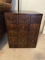 Front view of the teak cabinet showing 15 small drawers each with a single round wooden knob.