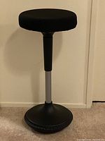 Front view of black ergonomic wobble stool with weighted base and silver adjustable column.