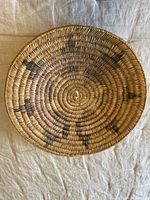 Top view of the indigenous shallow basket showing faint dark dyed patterns on natural fibers and central spiral weave.