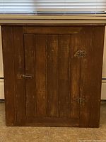 Front view of the wood cabinet with closed doors showing the antique wood finish and metal hardware.