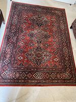 Full view of wool rug with red dominant color and multi-layered geometric border design.