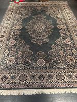 Full view of hunter green rectangular area rug with central medallion and fringe