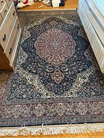 Full view of the rectangular area rug placed on a wood floor between furniture, showing its central medallion and patterned border.