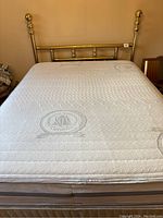 Full view of the queen size bed with brass headboard, mattress, and boxspring visible.