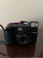 Front view of Canon Sure Shot with built-in flash, lens visible with 'Canon Lens 38mm 1:2.8 AUTO FOCUS' text.