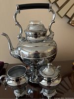 Front view of entire polished silver automatic coffee maker with ornate handle, along with matching cream and sugar set.