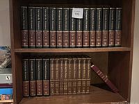 Wide shot of bookshelf displaying a full set of Encyclopedia Britannica volumes arranged in order from volume 1 to 32 with black and burgundy spines.