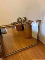 Full view of the rectangular gold-framed mirror leaning against a wall showing its overall condition and ornate design.
