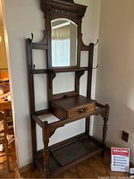 Full view of antique oak hall tree showing mirror, hooks, drawer, legs and lower shelf