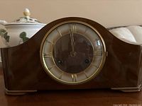 Front view of the clock showing wooden casing and gold Roman numeral dial under glass.