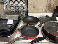 Displays all pans and cookware including muffin tin, pizza pan, frying pans with lids, and cooking racks arranged on a table.