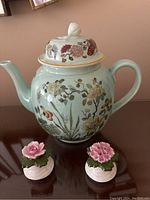 Full view of Ming Jade Calyx ware teapot with floral decoration and Aynsley floral salt and pepper shakers on dark reflective surface.