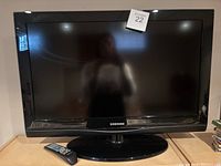 Front view of the Samsung 32 inch flat screen television showing the screen, bezel, stand, and remote placed in front.