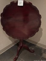 Front view of wooden pedestal tilt-top table showing the round scalloped edge top and tripod base with claw feet