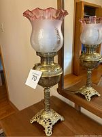 Full view of Victorian lamp showing pink ruffled etched glass shade and brass base standing on wooden surface