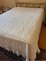 Full bed view showing white coverlet bedspread with textured pattern on queen or king size bed with brass headboard.