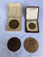 Four bronze medals arranged on a flat white background; two in boxes and two loose. Shows the variety and general condition of medals.