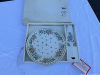 Top view of one cake plate and matching cake server in original box, showing floral design with pink and blue flowers and gold rim.