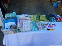 Photo showing organized quilting fabrics in blue and green colors, rotary cutter, scissors, quilting rulers and magazine booklets.