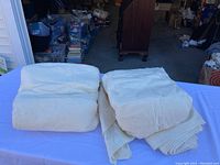 Two folded cream-colored blankets of quilt batting laid on a table.