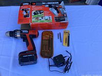 Black & Decker 12V cordless drill/driver and accessories including battery charger, screwdriver bit set in case, and DeWalt screwdriver bits pack, with original drill box
