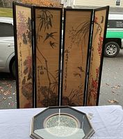 Four-panel Chinese wooden folding screen with painted floral and bird motifs outdoors on pavement.