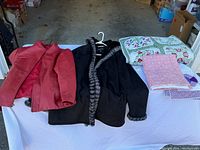 Red women's size 3X leather coat, black suede Jones New York coat with fur trim, Pegasus reversible quilt and two pillow shams laid out on table