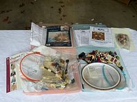 Two plastic storage kits containing cross stitch and needlepoint supplies including multiple floss skeins, hoops, fabric, and printed guides.