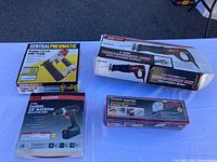 Four boxed power tools laid on a white table including air nailer/stapler, reciprocating saw, cordless drill/driver, and oscillating tool.