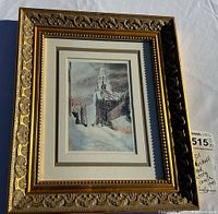 Overall view of framed wintery church print on a white surface showing gold detailed frame and slight shadow.