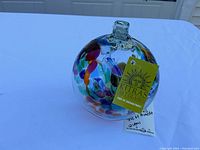 Clear glass art ball with colorful tree and leaf motifs and yellow Kitras Art Glass tag