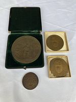 Four bronze medals displayed on white fabric; including large Henry Hudson medal in green velvet box, two portrait medals in white boxes, and one small round medal.