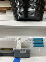 Black round plastic bucket on the top shelf, clear plastic container with blue sliding latches, and gray toolbox with yellow latch on lower shelf.