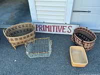 Overall lot showing the wooden sign and four baskets arranged on pavement outside of garage.
