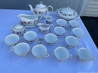 Full display of the Royal Doulton Roselle tea set components including cups, saucers, teapot, sugar bowl, creamer, covered serving bowl, and gravy boat on a white table.