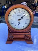 Front view of Seiko tabletop clock showing round face, wooden frame with carved decorations, and clock hands.