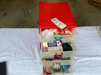 Plastic drawer unit with red lid containing sewing supplies such as ribbons, bias tape, and packaged notions.