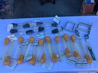 Multiple unopened turkey basters in clear plastic packaging on table, black and yellow bulb heads visible, along with some U-shaped metal brackets at the back.