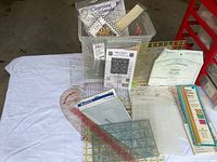 Top-down view of plastic bin containing various quilting cutting triangles, rulers, and paper templates arranged inside, placed on white cloth.