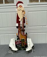 Full view of wooden Santa decoration with deer and Christmas sign, and pair of white figure skates placed on each side.