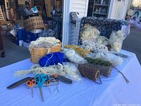 Wide photo showing numerous yarn and wool skeins and bundles in different colors and thicknesses alongside multiple pairs of scissors on a white cloth.