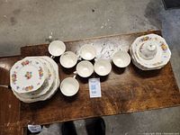 Top view of the full Wedgwood and Co. rose floral china set including cups, saucers, plates, and lidded butter dish arranged on a wooden table.