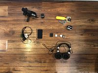 Photo showing all items for sale laid out on floor: video camcorder with grip, action camera with yellow float and batteries, two sets of headphones, old Motorola flip cellphone, various batteries and charging docks.